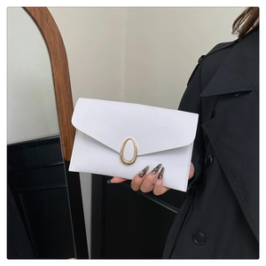 Détail d'une pochette enveloppe blanche avec boucle dorée tenue par un mannequin