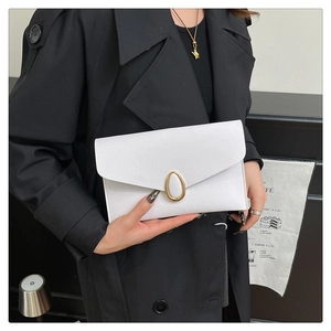 Détail d'une pochette enveloppe blanche avec fermoir doré portée avec un trench noir