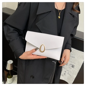 Gros plan d'une pochette enveloppe blanche avec boucle dorée tenue par un mannequin