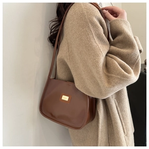 Detail of brown leather crossbody bag with golden plaque on tweed coat background