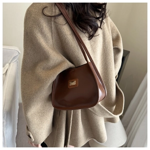 Close-up of brown synthetic leather shoulder bag with metallic plaque on model