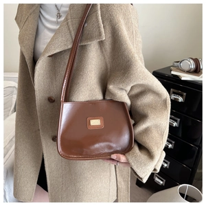Detail of dark brown leather underarm bag featuring a gold logo plate and sleek finish