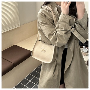 Detail of a beige minimalist leather shoulder bag with a gold metal logo plate for women