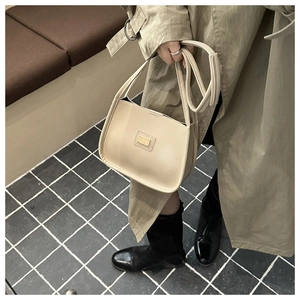 Detail of minimalist cream leather bag with metal logo and versatile shoulder strap