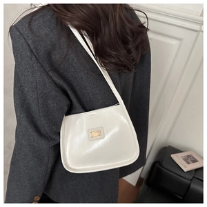 Close-up of cream white glossy leather shoulder bag with gold square metal logo buckle