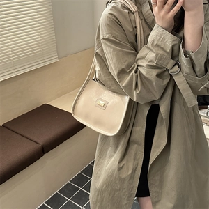 Minimalist cream shoulder bag with metallic logo detail shown in artistic shadow lighting