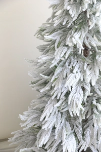 Close-up of realistic snow-flocked PE needles on a green artificial Christmas tree branch