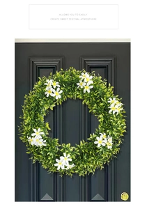Détail d'une couronne de feuilles vertes artificielles avec fleurs blanches sur porte grise