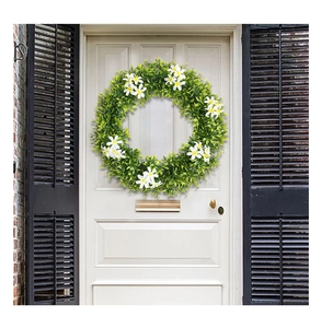 Détail d'une couronne verte artificielle avec marguerites sur une porte en bois