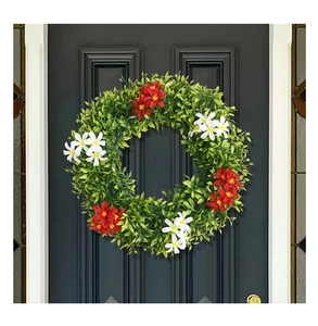 Close-up of artificial eucalyptus wreath with red and white flowers on a grey door