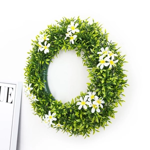 Couronne printanière de feuilles vertes artificielles avec fleurs blanches sur mur blanc