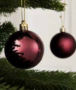 Close-up of matte and glossy burgundy Christmas ornaments hanging on a green tree branch