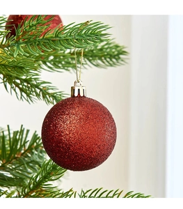 Dettaglio di una palla di Natale rossa glitterata appesa a un ramo di albero festivo