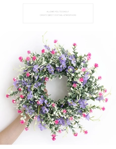 Detail of purple wildflower wreath with green leaves held against a white background