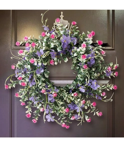 Detailed view of a purple and pink wildflower wreath on a dark wooden door with a knocker