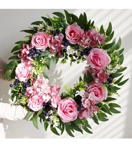 Detail of pink faux roses and eucalyptus wreath held against a white wall with shadows