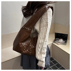 Close-up of a brown tote bag with star rivets on shoulder and office props background