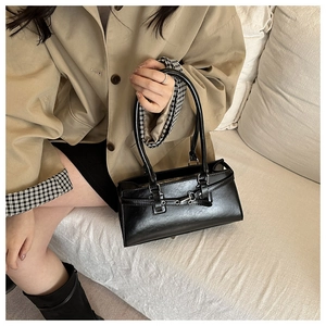 Detail of a minimalist black baguette shoulder bag with silver metallic buckle and leather texture