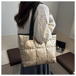 Detailed view of champagne gold quilted tote bag with black strap worn by a model