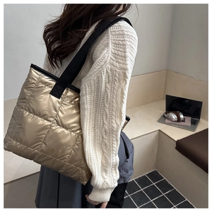 Detail view of gold quilted puffer tote bag with wide black strap and large square texture