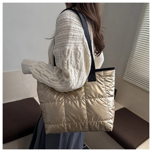 Close-up of golden quilted puffer tote bag with wide black strap on female model
