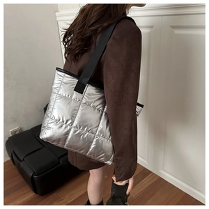 Silver quilted tote bag with black strap worn by a model in a minimalist modern setting