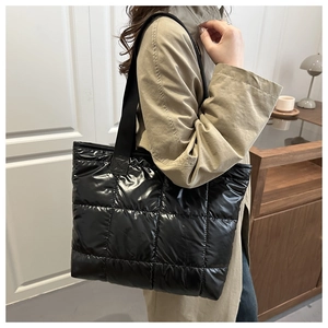 Close-up of black quilted puffer tote bag with glossy finish and wide textile strap