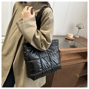 Detail of a black quilted tote bag with a glossy finish and a stylish wide shoulder strap