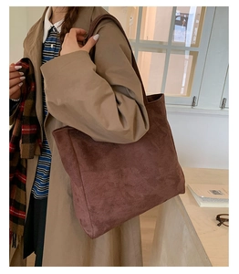 Close-up of a large brown suede tote bag worn on shoulder in a minimalist room