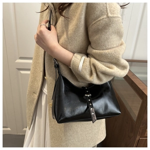 Detail of black glossy faux leather shoulder bag with silver buckle and metal rivets
