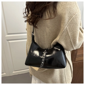 Detail view of black glossy underarm bag with silver rivets on a beige coat