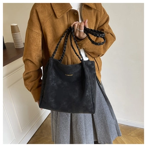 Detail of black suede tote bag with woven handles and golden logo text on matte surface