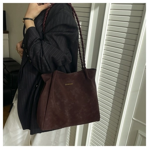 Detail of burgundy tote bag featuring hand-woven braided handles and a gold foil logo
