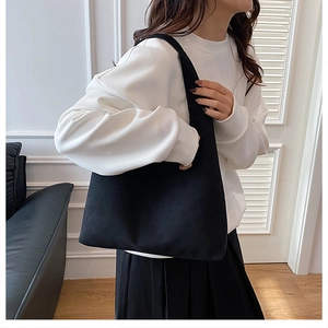 Minimalist black canvas tote bag shown on shoulder with clean casual outfit
