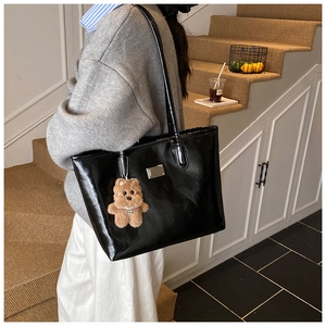 Glossy black tote bag with silver plaque and plush bear charm in a lifestyle setting