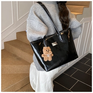 Close-up of shiny black patent leather tote bag featuring a cute brown plush bear charm