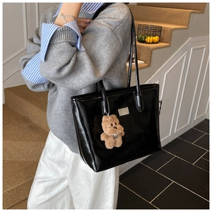 Detail of black patent leather tote bag featuring metal logo and plush bear charm