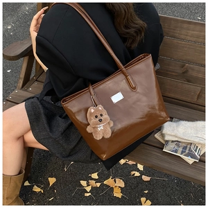 Detail view of large brown faux leather tote bag with cute bear charm and metal hardware