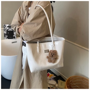 Detailed side view of a white glossy tote bag with a cute brown teddy bear charm