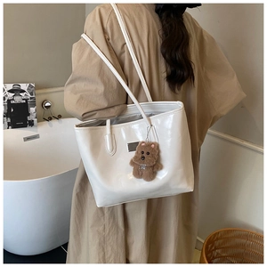 Detail of white glossy tote bag with slim straps and a cute plush bear pendant