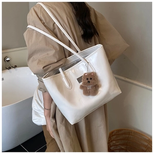 Detailed back view of a white glossy tote bag featuring a cute brown plush bear charm