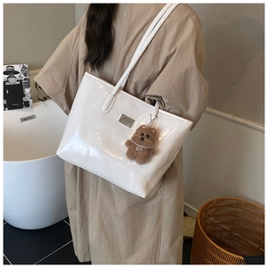 White glossy leather tote bag with plush bear charm and metal logo plate detail