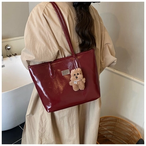 Close-up of a burgundy patent leather tote bag with a metallic plate and plush bear charm