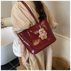 Close-up of wine red patent leather tote bag with cute plush bear charm and metal plate
