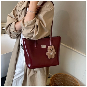 Detail of burgundy glossy tote bag with silver plaque and plush bear charm on model