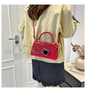 Detail of red crocodile embossed patent leather handbag with black buckle and strap