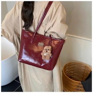 Detail of burgundy glossy patent leather tote bag with metallic plaque and bear charm