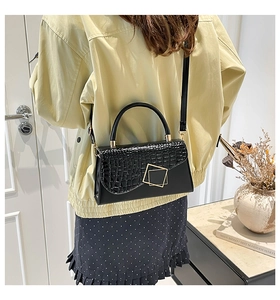 Model wearing a black crocodile embossed small square bag with golden lock detail
