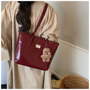Detail of dark red patent leather tote bag with metallic logo and plush bear charm