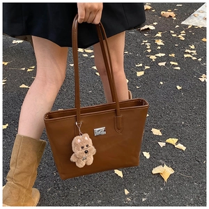Brown tote bag with cute dog charm shown in an autumn street setting with gingko leaves